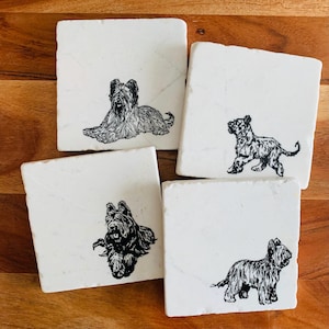 May include: Set of four white marble coasters with black line drawings of dogs. Each coaster features a different breed of dog.