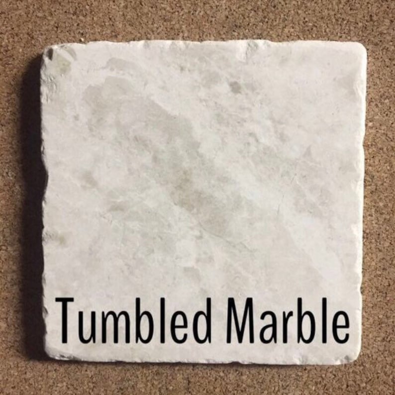 May include: A close-up of a white tumbled marble tile. The tile has a rough, textured surface and is slightly irregular in shape. The text "Tumbled Marble" is printed in black at the bottom of the tile.