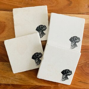 May include: Set of four white square coasters with black and white illustrations of a dog's head on each coaster.