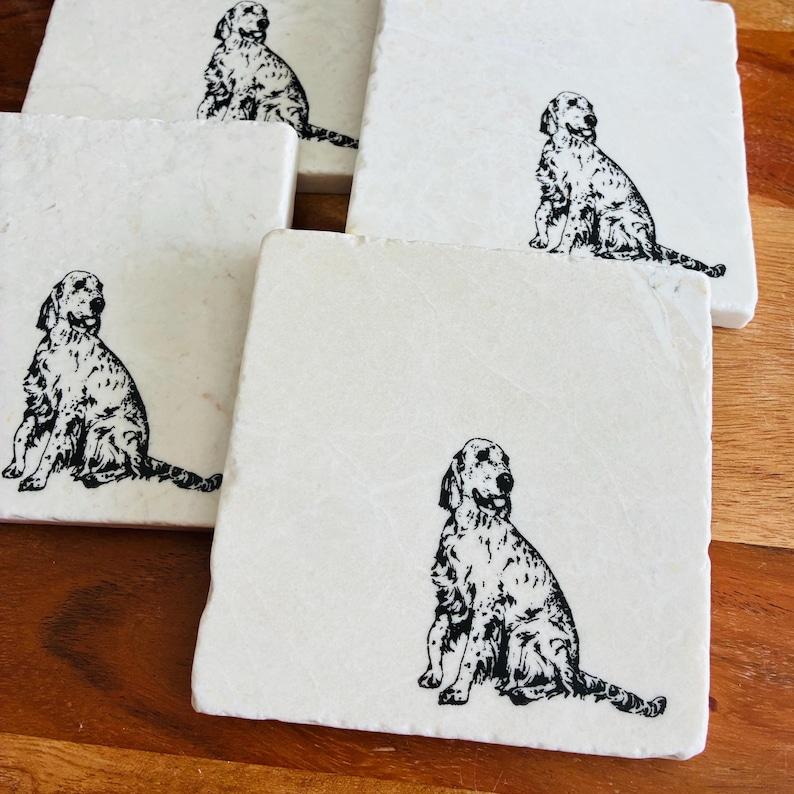 以下が含まれることがあります： 犬の黒いシルエット画像が描かれた白い大理石コースター4枚セット。各コースターには、犬の異なるポーズが描かれています。