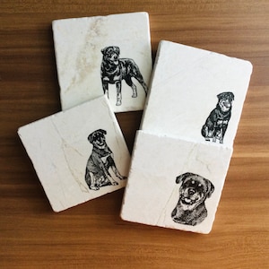 May include: Four white marble coasters with black and white images of Rottweilers. Each coaster features a different pose of the dog.