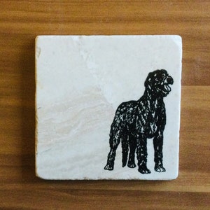 May include: A black and white silhouette of a dog on a white square coaster.