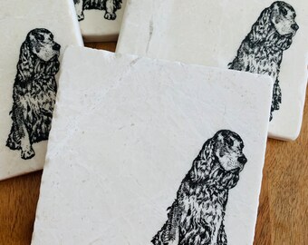 May include: Four white square coasters with black and white illustrations of a dog on each. The coasters are made of marble.
