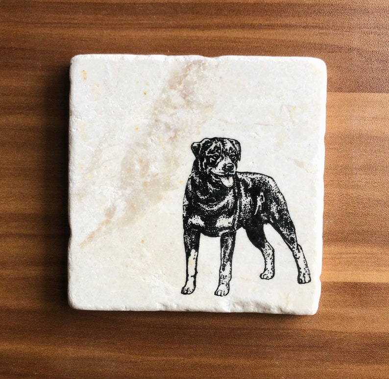 May include: A white marble coaster with a black and white illustration of a Rottweiler dog.