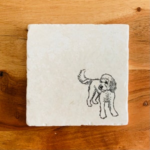 May include: White marble coaster with a black line drawing of a dog on it.