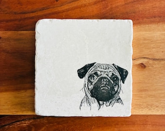 May include: Square, off-white stone coaster featuring a black and white illustration of a pug dog's face. The coaster is set against a wooden background. The pug's face is detailed with wrinkles and a focused expression. A decorative item for home decor.