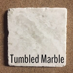 May include: A close-up of a white, tumbled marble tile. The tile has a rough, textured surface. The text "Tumbled Marble" is printed on the tile.