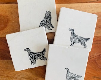 May include: Four white square coasters with black and white illustrations of Irish Setter dogs. The coasters are made of marble and have a smooth, polished surface.