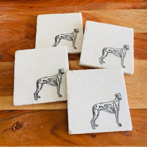 Op de afbeelding: Set van vier vierkante witte marmeren onderzetters. Elke onderzetter heeft een zwart-wit illustratie van een hond. De onderzetters zijn gerangschikt op een houten oppervlak, wat hun ontwerp en textuur laat zien.