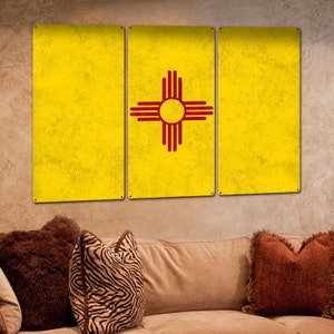 May include: Three metal panels with a distressed yellow background. The center panel features the state flag of New Mexico, which is a red Zia symbol on a yellow background. The panels are hanging on a wall.