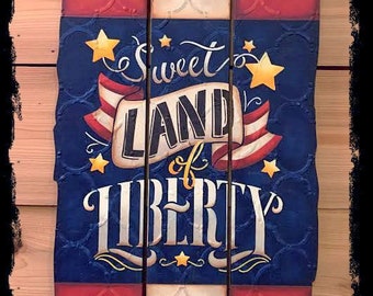 May include: A wooden sign with a red, white, and blue American flag design. The sign reads "Sweet Land of Liberty" with gold stars and a red, white, and blue ribbon. The sign is hanging from a red, white, and blue rope.