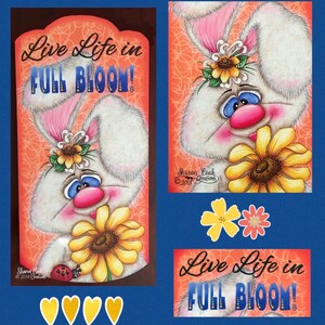 Op de afbeelding: Een wit konijn met roze oren houdt een gele zonnebloem vast. Het konijn draagt een zonnebloemenkroon. De achtergrond is oranje met een swirl-patroon. De tekst "Live Life in Full Bloom!" staat in blauwe en gele letters op een wit banner.
