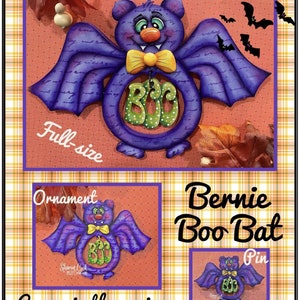Op de afbeelding: Een paarse vleermuis met een gele strik en het woord "BOO" op zijn borst. De vleermuis is verkrijgbaar in drie maten: vol formaat, ornament en speld. De vleermuis is een Halloween-decoratie.