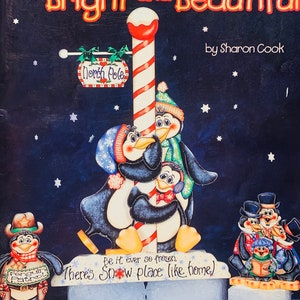 May include: A colorful illustration of penguins on a snowy background. The penguins are standing on ice blocks and are holding a sign that says "Be it ever so frozen, there's snow place like home".