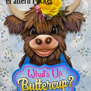 May include: A wooden cutout of a Highland cow with a yellow flower and pink bow on its head. The cow is holding a blue sign with the text "What's Up Buttercup?" in gold letters. The sign has a pink border and gold stars.