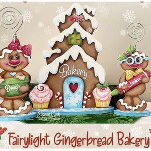 May include: A festive gingerbread bakery scene featuring a gingerbread house, two gingerbread figures, and cupcakes. The bakery has a heart-shaped door and the word "Bakery". The gingerbread figures hold a bowl of dough and a rolling pin. The text "Fairylight Gingerbread Bakery" is at the bottom.