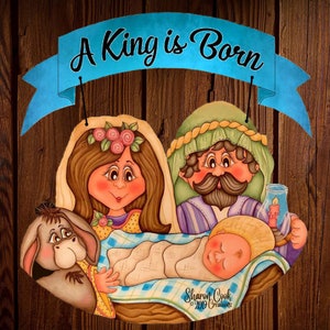 Può includere: Uno striscione blu con il testo "A King is Born" è appeso sopra una scena della Natività con Maria, Giuseppe, Gesù bambino e un asino. La scena è dipinta in uno stile cartone animato con colori vivaci.