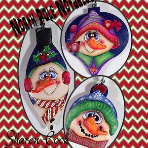 Puede incluir: Tres adornos de muñeco de nieve pintados a mano con diferentes expresiones faciales y sombreros. Los adornos están decorados con pintura roja, verde, azul y blanca. Los adornos están etiquetados como "North Pole Notables" y "Sharon Cook Creations 2013".