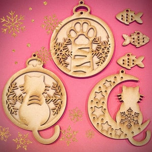 May include: Set of five unfinished wooden ornaments shaped like a paw print, a crescent moon, a cat, and two fish. The ornaments are ready to be painted or decorated.
