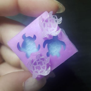 May include: A purple silicone mould with four turtle shapes. The turtles are outlined in a lighter shade of purple and have a textured shell design.