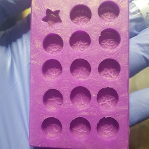 May include: Purple silicone mould with 16 circular cavities and one star-shaped cavity. Each circular cavity has a different design.