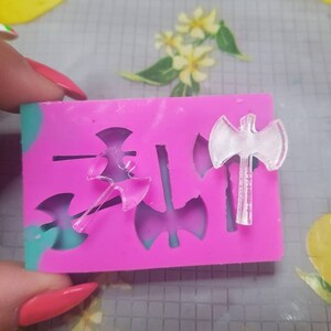 May include: A pink silicone mould with four axe shapes. The mould is designed to create resin crafts.