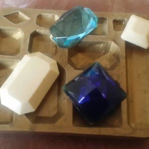 Op de afbeelding: Een messing dienblad met meerdere vakken, elk met een edelsteen in een andere kleur. De edelstenen zijn lichtblauw, donkerblauw en wit.