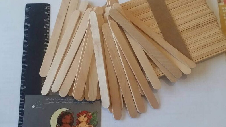 K&ouml;nnte beinhalten: Ein gro&szlig;er Stapel nat&uuml;rlicher Holz-Bastelst&auml;bchen, etwa 100 St&auml;bchen, mit abgerundeten Enden. Die St&auml;bchen sind f&auml;cherf&ouml;rmig angeordnet, wobei sich einige St&auml;bchen &uuml;berlappen.