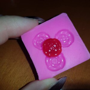 Pode incluir: Forma de silicone rosa com três impressões circulares, uma das quais tem um doce vermelho.