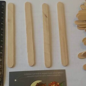 K&ouml;nnte beinhalten: Vier Holzst&auml;bchen zum Basteln, etwa 15 cm lang, sind in einer Reihe auf einer wei&szlig;en Oberfl&auml;che angeordnet. Links im Bild ist ein Lineal zu sehen. Rechts im Bild ist ein Stapel &auml;hnlicher Holzst&auml;bchen zu sehen.