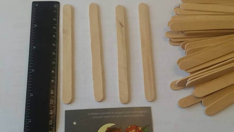 K&ouml;nnte beinhalten: Vier Holzst&auml;bchen zum Basteln, etwa 15 cm lang, sind in einer Reihe auf einer wei&szlig;en Oberfl&auml;che angeordnet. Links im Bild ist ein Lineal zu sehen. Rechts im Bild ist ein Stapel &auml;hnlicher Holzst&auml;bchen zu sehen.
