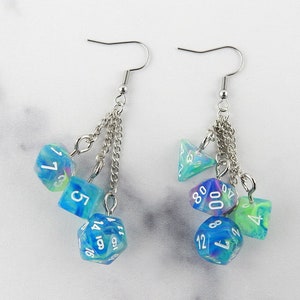 May include: A pair of silver dangle earrings with a chain and multiple blue and green iridescent dice charms. The dice have white numbers.