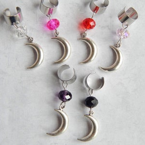 May include: Six silver crescent moon earrings with different colored crystal beads. The earrings are made of metal and have a clip-on design.