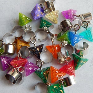May include: A selection of colourful, polyhedral dice rings in shades of green, purple, orange, and blue. Each die is connected to a silver-toned adjustable ring. The dice have white numbering.