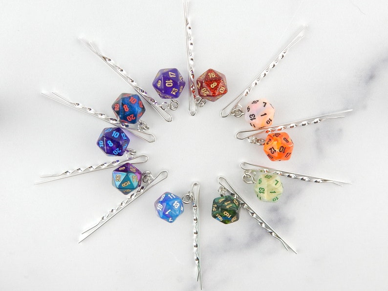 Op de afbeelding: Tien zilveren haarclips met iriserende dobbelstenen bedels. Elke dobbelsteen is van een andere kleur en heeft zwarte cijfers. De dobbelstenen zijn ongeveer 2,5 cm in diameter.