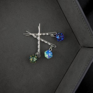 Op de afbeelding: Drie zilveren haarclips met iriserende dobbelstenen bedels. De dobbelstenen zijn blauw, groen en zwart met gouden cijfers.