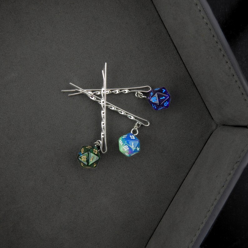 Op de afbeelding: Drie zilveren haarclips met iriserende dobbelstenen bedels. De dobbelstenen zijn blauw, groen en zwart met gouden cijfers.