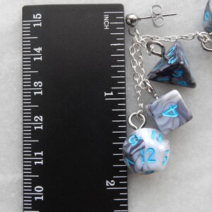 Op de afbeelding: Een paar zilveren oorhangers met een ketting en vier zwarte en witte swirl-dobbelstenen bedels. De dobbelstenen hebben blauwe nummers. De oorringen zijn ongeveer 3,8 cm lang.