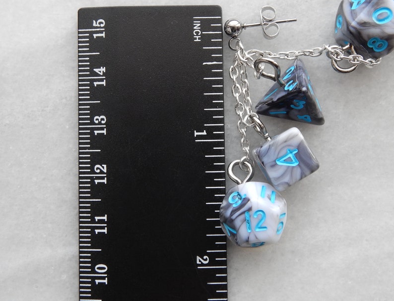 Op de afbeelding: Een paar zilveren oorhangers met een ketting en vier zwarte en witte swirl-dobbelstenen bedels. De dobbelstenen hebben blauwe nummers. De oorringen zijn ongeveer 3,8 cm lang.