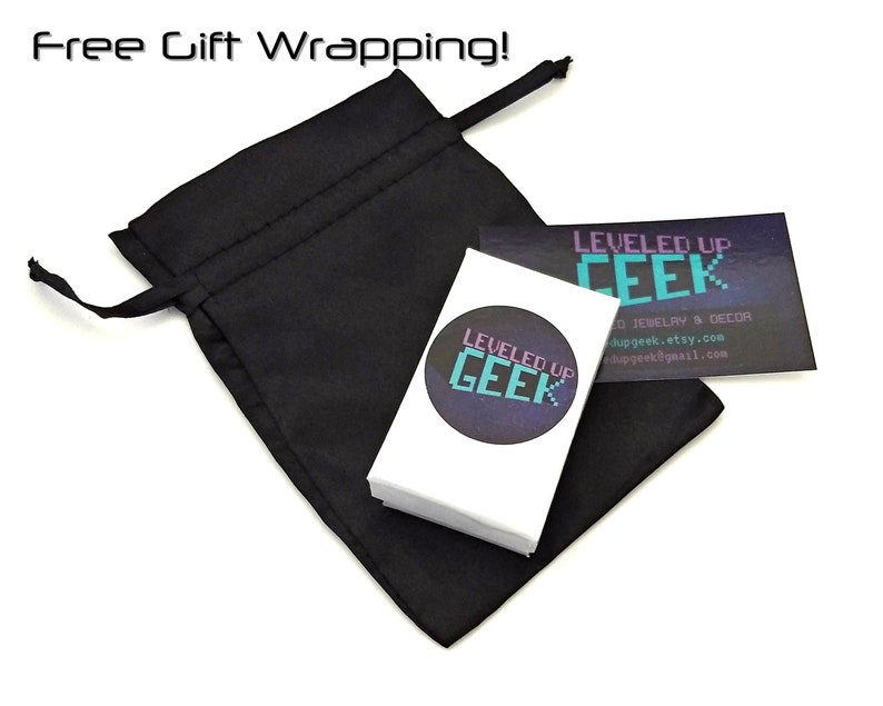 Op de afbeelding: Een zwarte trekkoordtas met een witte kaart erin. De kaart heeft een paars en turquoise logo met de tekst "LEVELED UP GEEK" en bevat de tekst "O JEWELRY & DECOR", "dupgeek.etsy.com" en "dupgeek@gmail.com".
