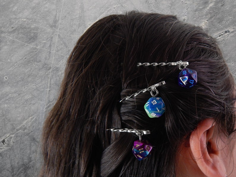 Op de afbeelding: Drie zilveren haarclips met iriserende dobbelstenen bedels. De dobbelstenen zijn blauw, groen en paars met witte cijfers.