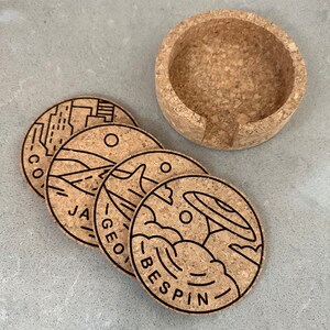 May include: Four cork coasters with black outlines of different designs. The coasters feature the words "CO", "JA", "GEO", and "BESPIN".