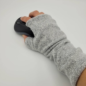 May include: A gray fingerless glove with a ribbed texture. The glove is worn on a hand holding a black computer mouse.
