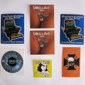 May include: A collection of nine stickers featuring various designs. The stickers include a blue sticker with the text "Southern Culture On The Skids", a yellow sticker with the text "FOREKONS" and Russian text, a red sticker with the text "BLACK LABEL SOCIETY THE BLESSED HELLRIDE", a blue sticker with an eye and the text "FLAT DUO JETS Lucky Eye", and two stickers with the text "Lords of Acid PUSSY" featuring a cat image.
