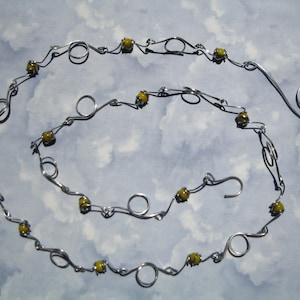 May include: A silver wire necklace with yellow glass beads. The necklace is made of wire that is twisted and shaped into loops and swirls. The necklace is about 20 inches long.