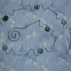 May include: A silver wire necklace with a spiral design and green and blue glass beads.