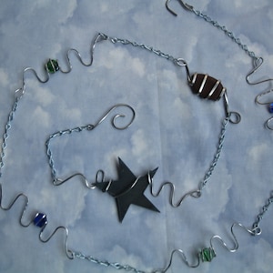 May include: A silver chain with a star-shaped pendant, a brown rock wrapped in wire, and blue and green glass beads.