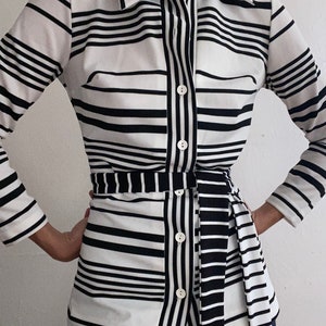 May include: A black and white striped button-down shirt with a matching belt. The shirt features a collared neckline, long sleeves, and a fitted silhouette. The stripes are horizontal and vertical, creating a bold pattern. The belt cinches the waist.
