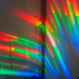 May include: A white door and wall are illuminated with vibrant streaks of light in a spectrum of colors, including red, orange, yellow, green, and blue. The light creates a dynamic and colorful display across the surfaces.