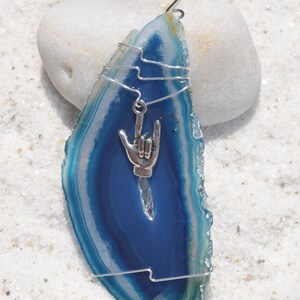 以下が含まれることがあります： 銀色のワイヤーで包まれた青いアゲートのスライスオーナメントと、銀色の「愛してる」の手のサインチャーム。